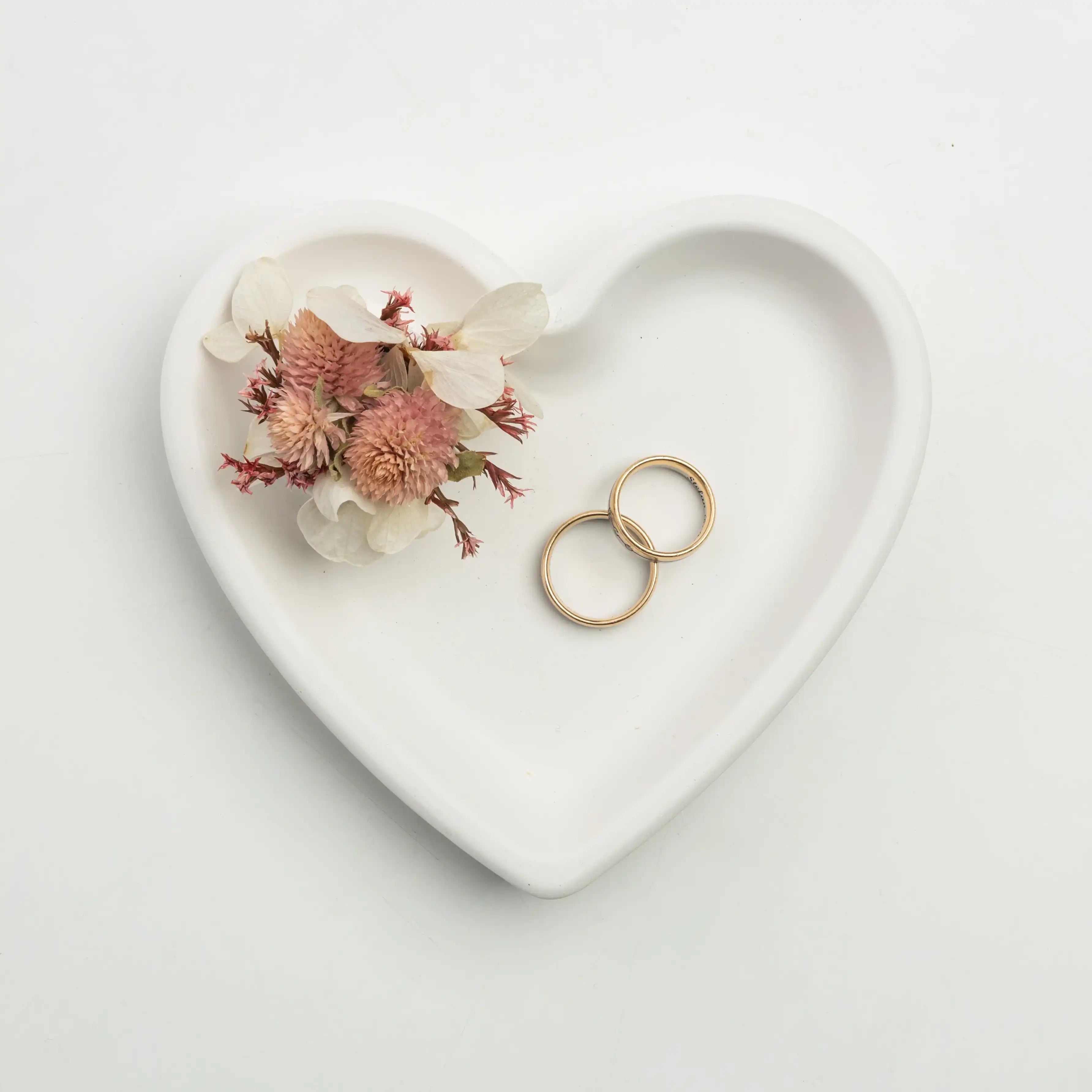 Herzförmige Schale mit Trockenblumen und goldenen Ringen
