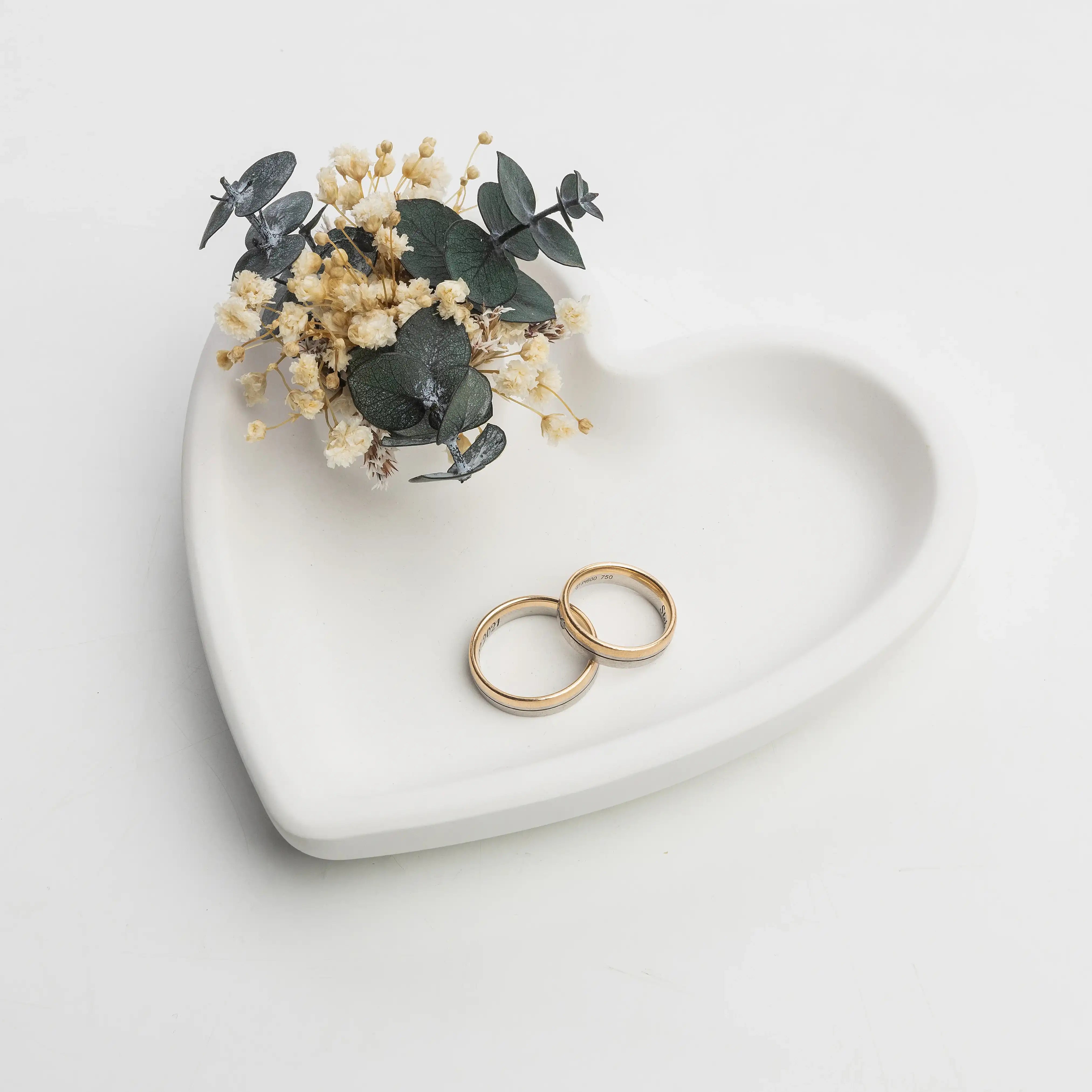 Handgefertigte Hochzeitsringe aus Gold und Silber mit Trockenblumen auf Herzschale