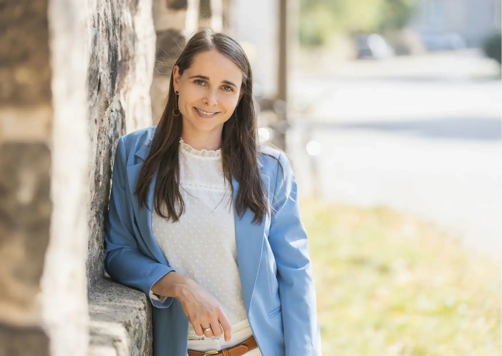 Frau in blauem Blazer und weißem Poloshirt lehnt an Steinmauer